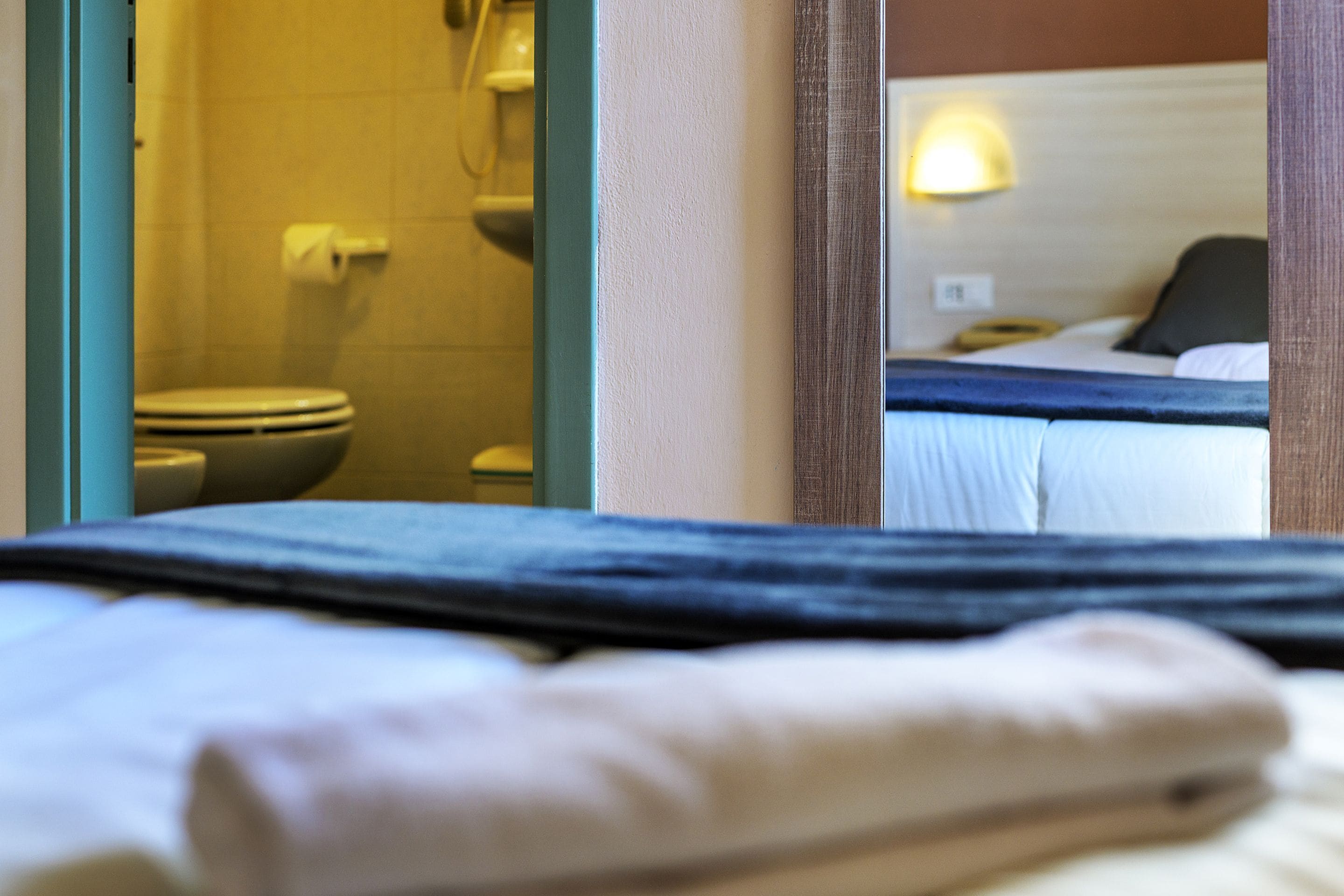 A hotel room with a bed, a visible bathroom with a toilet, and a mirror reflecting the room.
