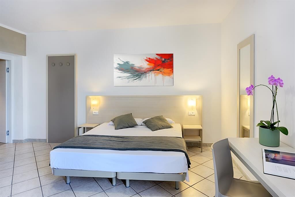 A modern hotel room with a bed, bedside tables, a desk, and a potted orchid.