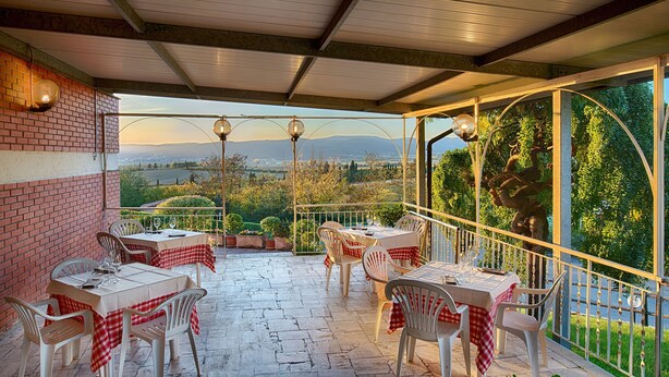Une terrasse extérieure couverte, dotée de tables et de chaises, un mur en briques et une vue sur la campagne.