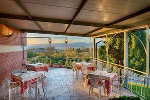 A covered outdoor patio with tables and chairs, a brick wall, and a view of the countryside.