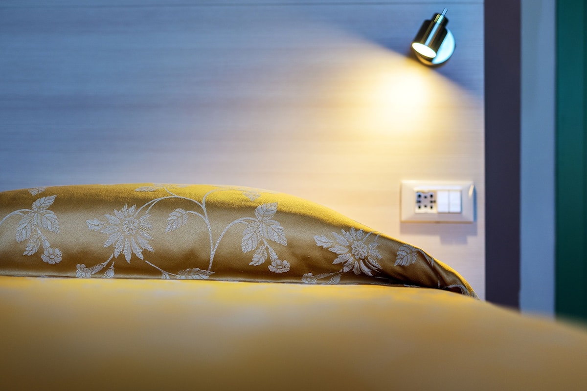 A bed with a floral-patterned blanket and a wall-mounted light fixture.
