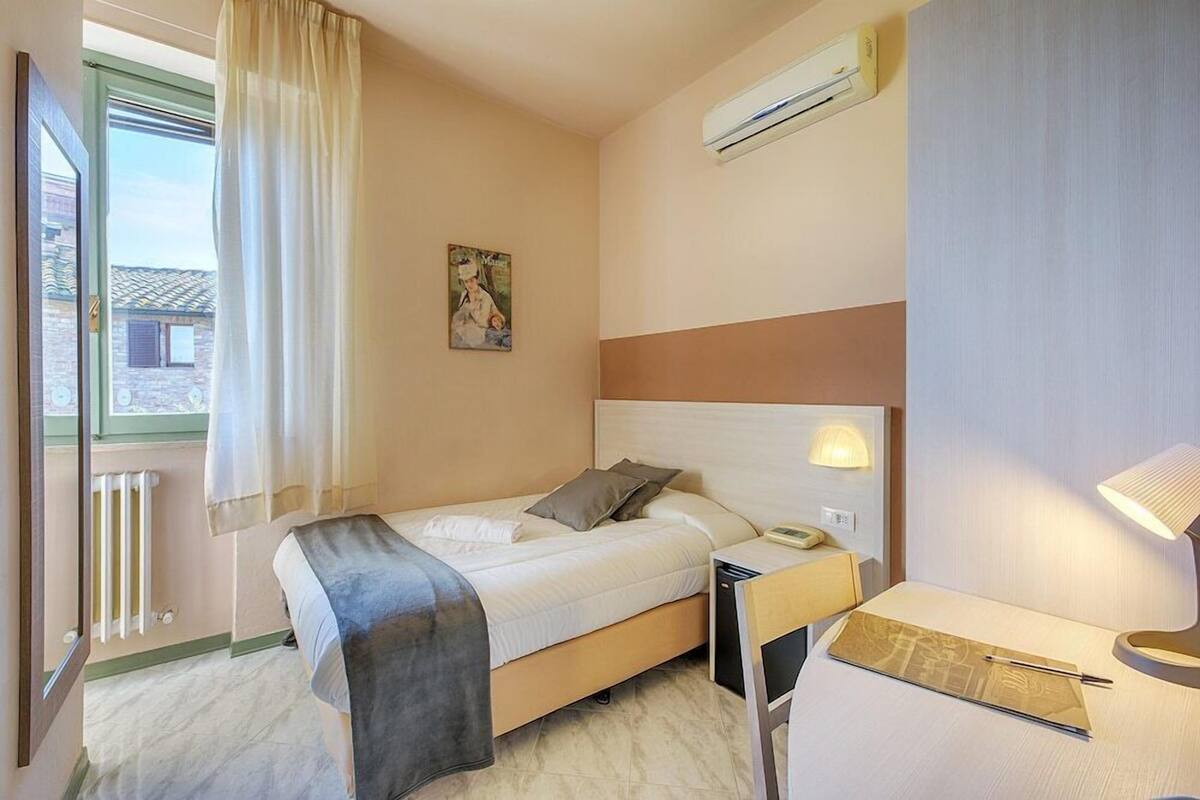 A hotel room with a bed, bedside table, lamp, and a window with curtains.