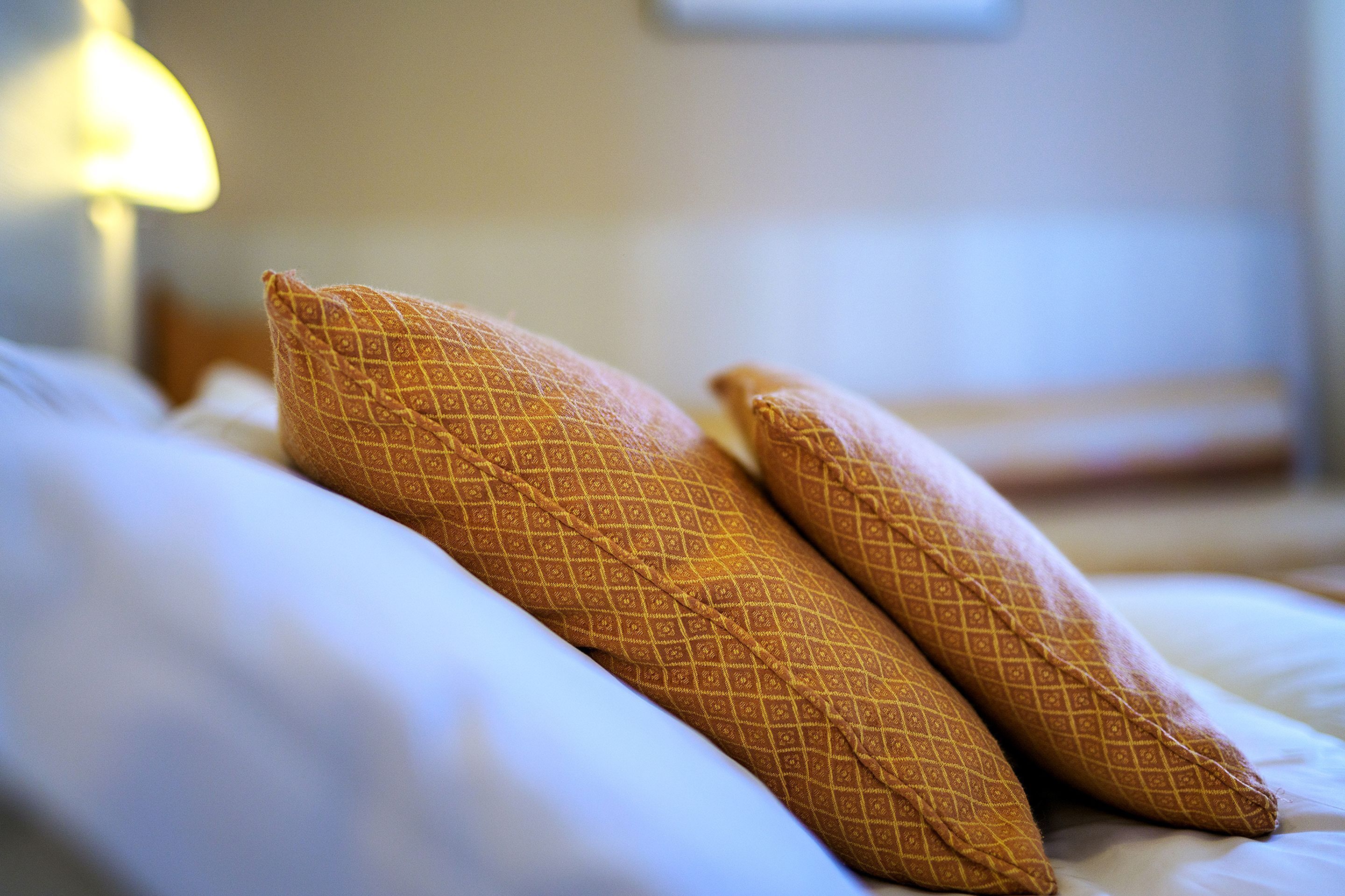 A bed with two pillows and a lamp in the background.