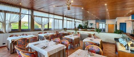 Un restaurant avec un plafond en bois, de grandes fenêtres et des tables dressées pour le service.