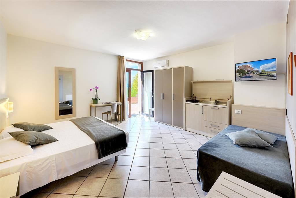 A hotel room with two beds, a desk, a wardrobe, and a television.