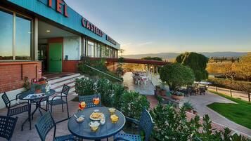 Une vue de l’extérieur d’un hôtel, avec des places assises en plein air, une vue sur la campagne et une enseigne indiquant « Hôtel Castillo, restaurant ».