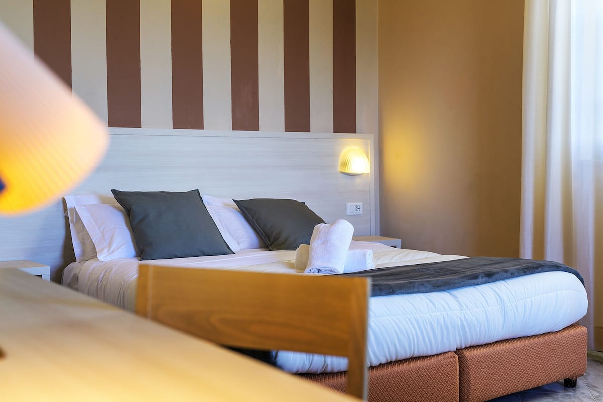 A neatly made bed with pillows and a blanket, a bedside lamp, and a wall with vertical stripes.