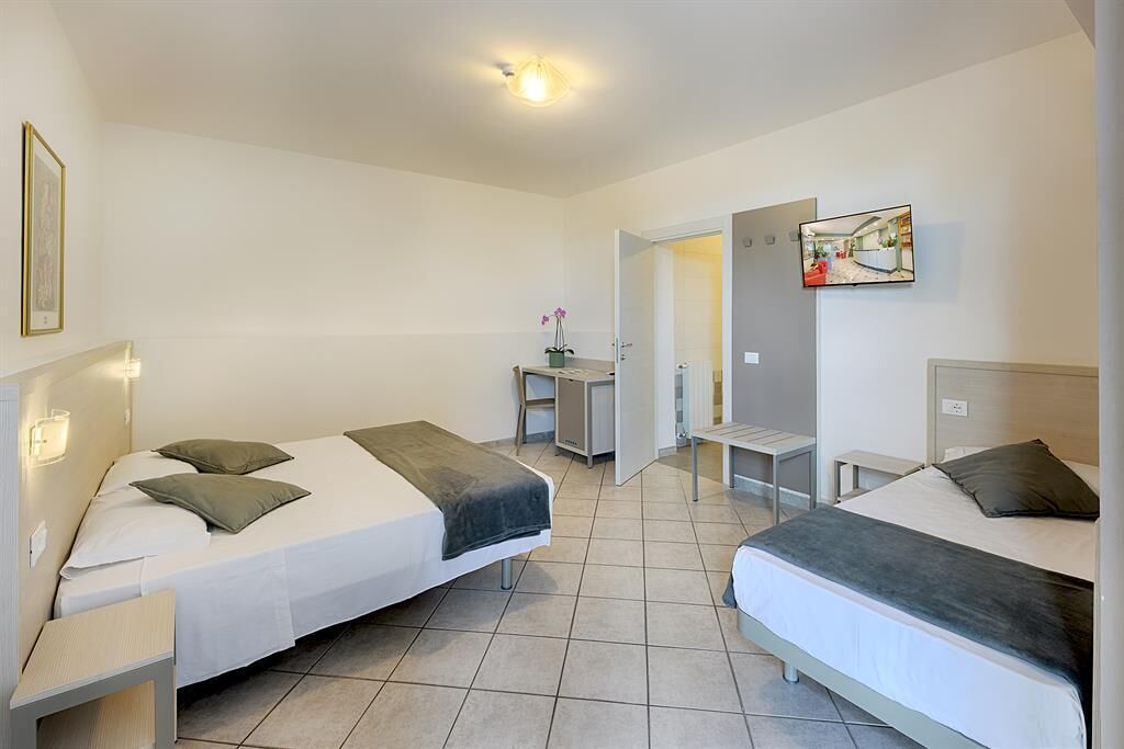 A hotel room with two beds, a desk, a chair, and a TV.