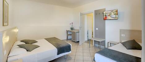 A hotel room with two beds, a desk, a chair, and a TV.