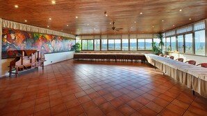 Une pièce spacieuse avec une longue table dressée pour le repas, de grandes fenêtres offrant une vue dégagée et un ventilateur de plafond.