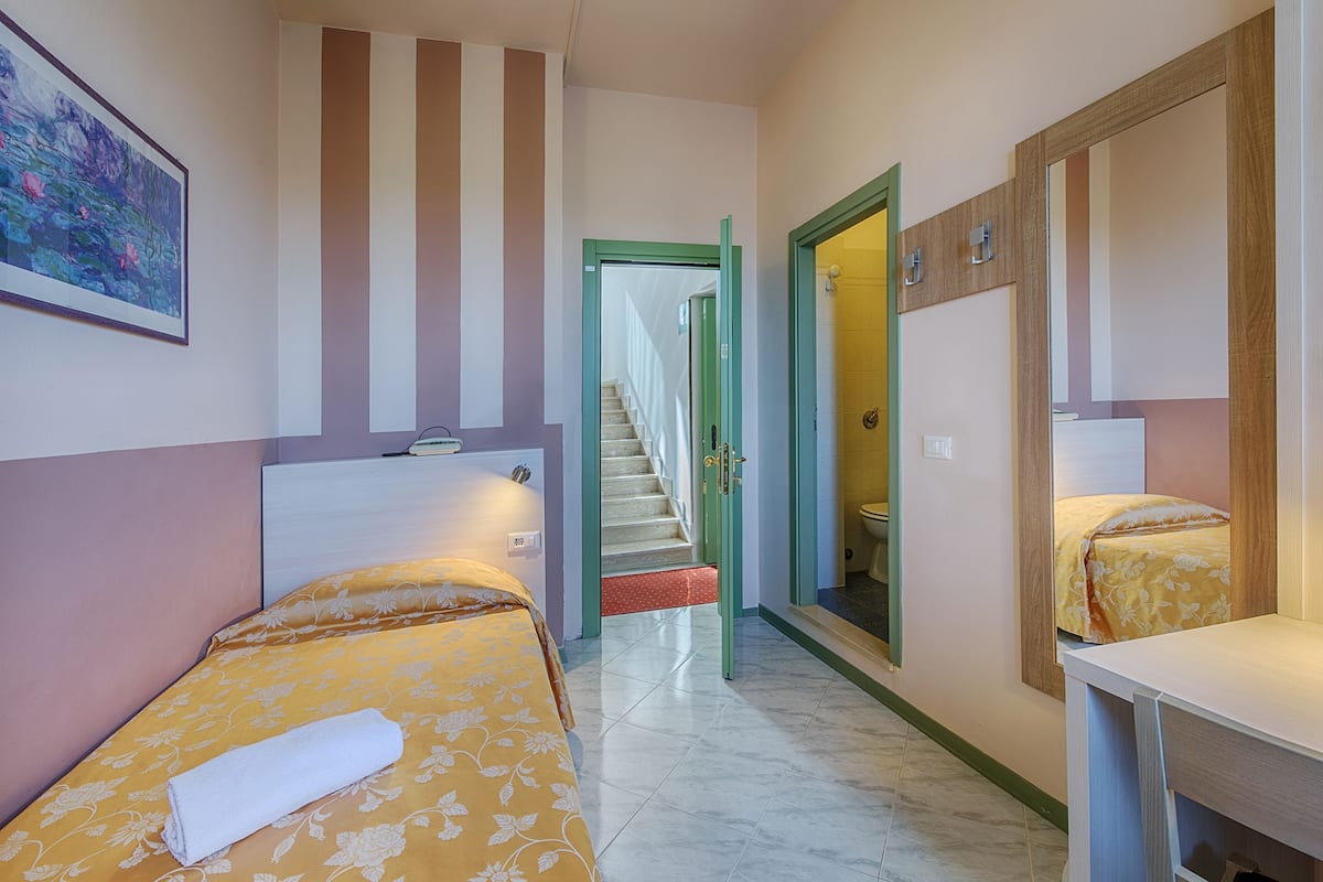 A hotel room with a bed, a desk, a bathroom with a toilet, and a staircase leading to another floor.