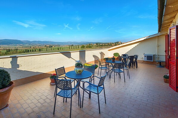 A terrace with outdoor seating, a view of the countryside, and a red door.