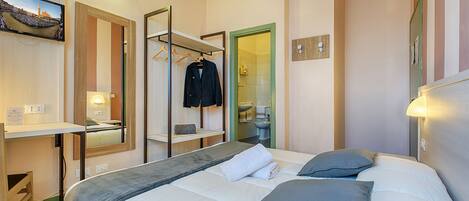 A hotel room with a bed, a desk, a mirror, a TV, and a bathroom visible through an open door.