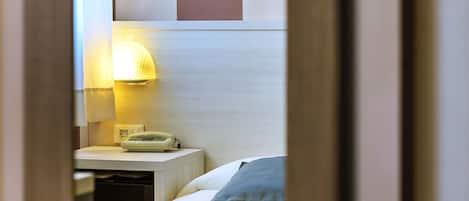 Habitación de hotel con cama, mesita de noche con lámpara y espejo que refleja la habitación.