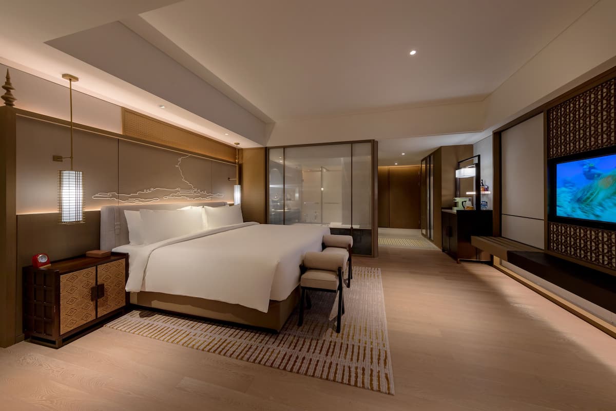 A modern hotel room with a large bed, a TV, a desk, and a walk-in closet.