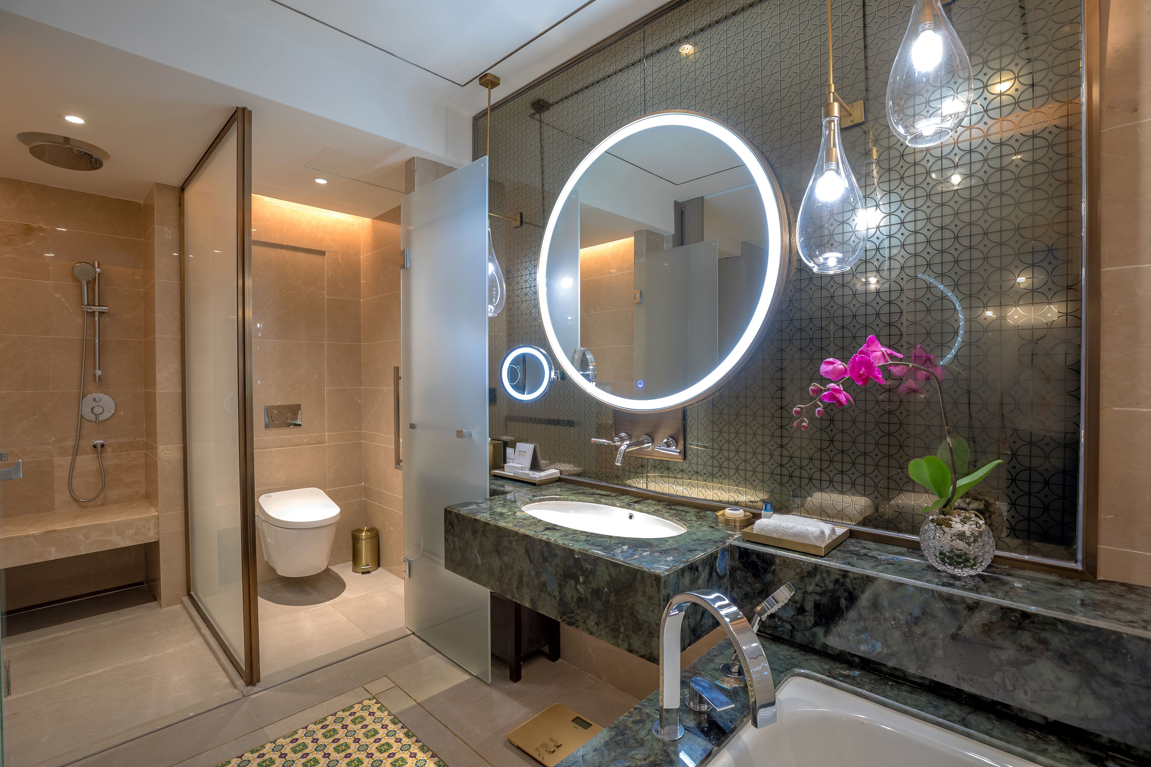 A modern bathroom with a glass-enclosed shower, a marble sink, and a large mirror with integrated lighting.