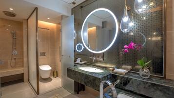 A modern bathroom with a glass-enclosed shower, a marble sink, and a large mirror with integrated lighting.