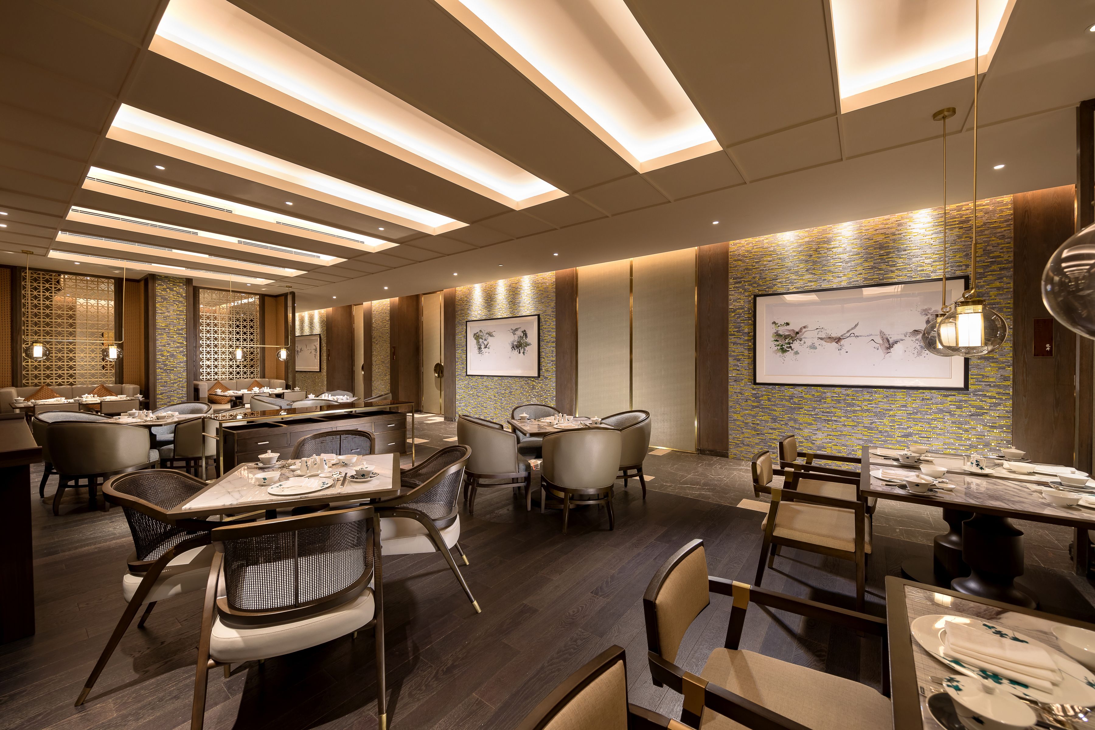 A modern dining area with multiple tables and chairs, recessed ceiling lighting, and decorative wall art.