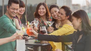 A group of people toasting with drinks at a table with a city view in the background.