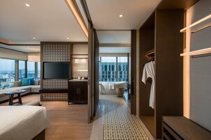 Una habitación de hotel moderna con una cama grande, un sofá, un televisor, un baño con bañera y vistas a la ciudad.