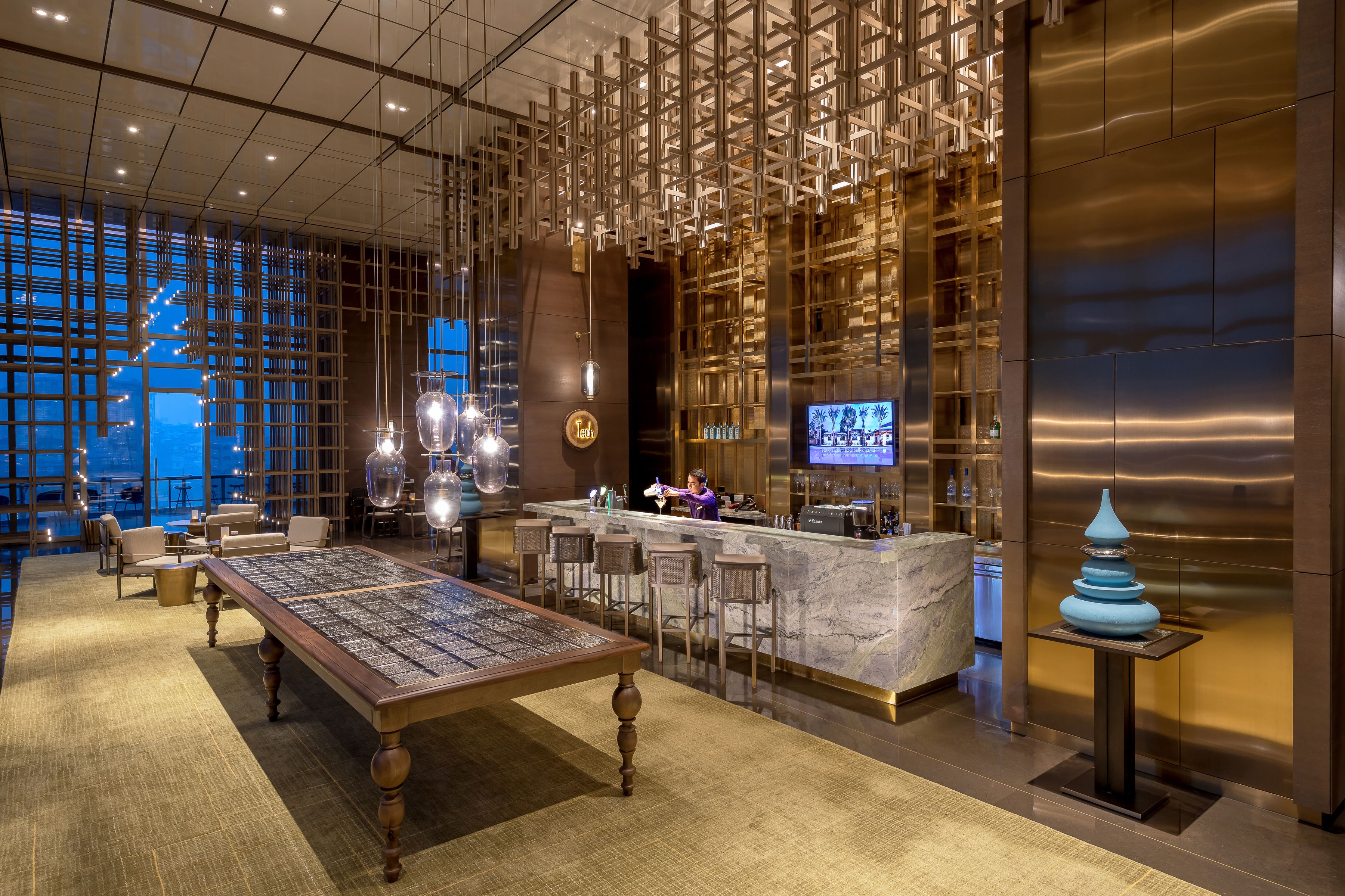 A modern bar area with a long table, bar stools, and a TV screen.