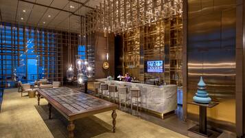 A modern bar area with a long table, bar stools, and a TV screen.