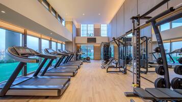 A gym with treadmills, weight machines, and a large window offering a view of the city.