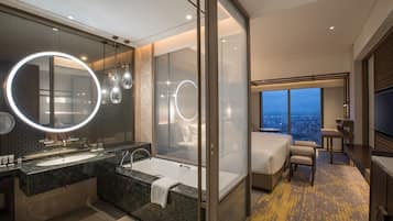 Un baño de hotel moderno con un espejo grande, una bañera y una ducha. En la habitación hay una cama y un televisor.