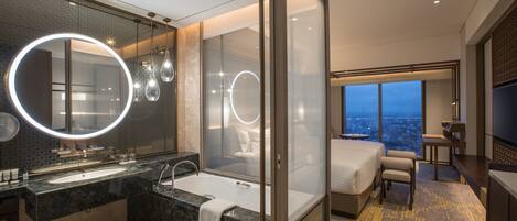 Un baño de hotel moderno con un espejo grande, una bañera y una ducha. En la habitación hay una cama y un televisor.