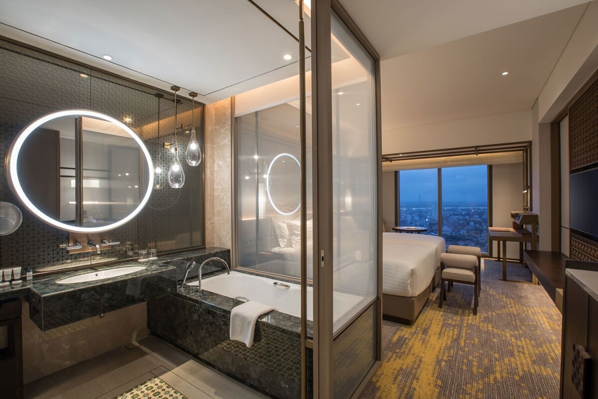 A modern hotel bathroom with a large mirror, a bathtub, and a shower.