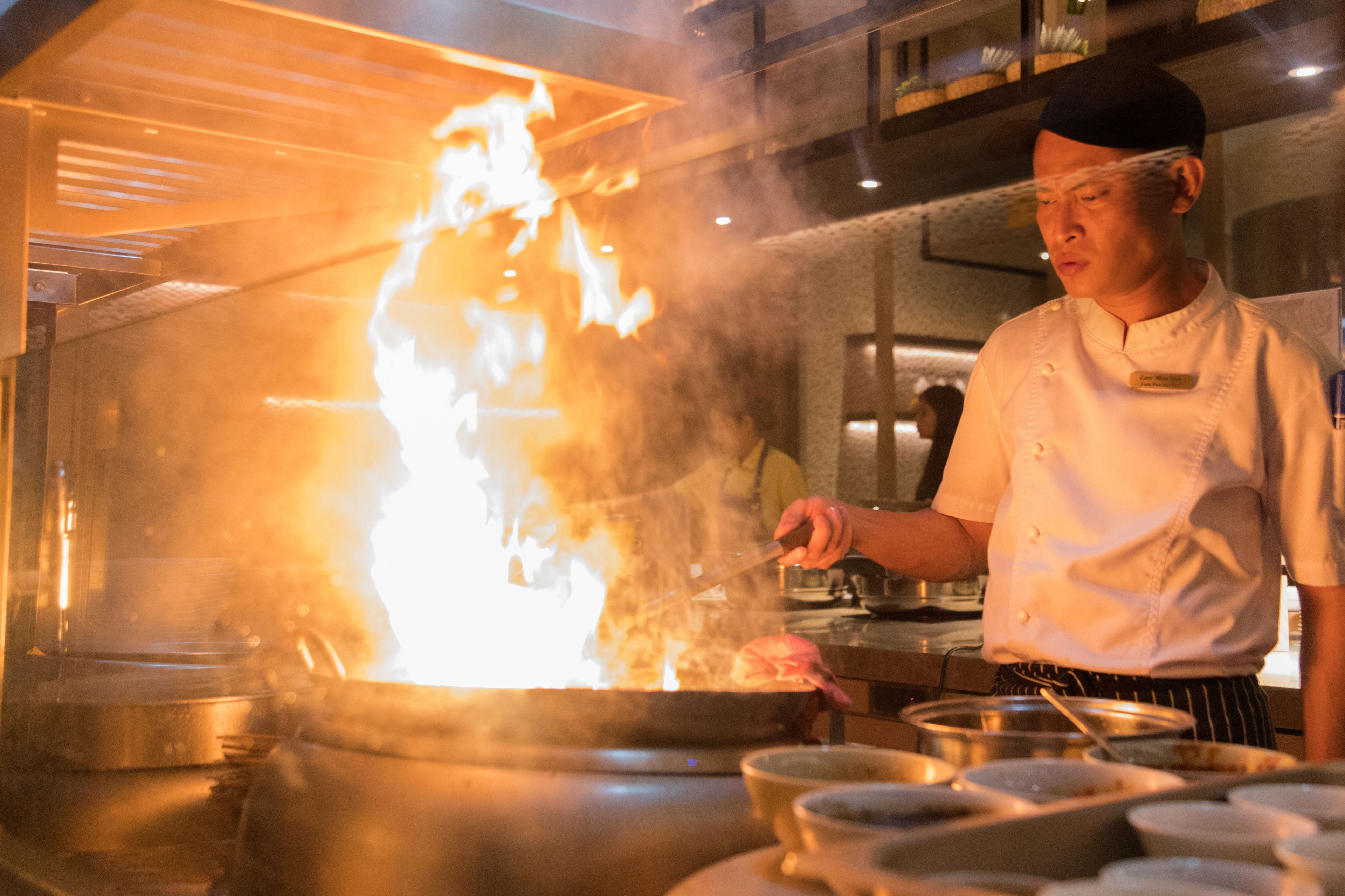 A chef cooking with a large flame in a professional kitchen.