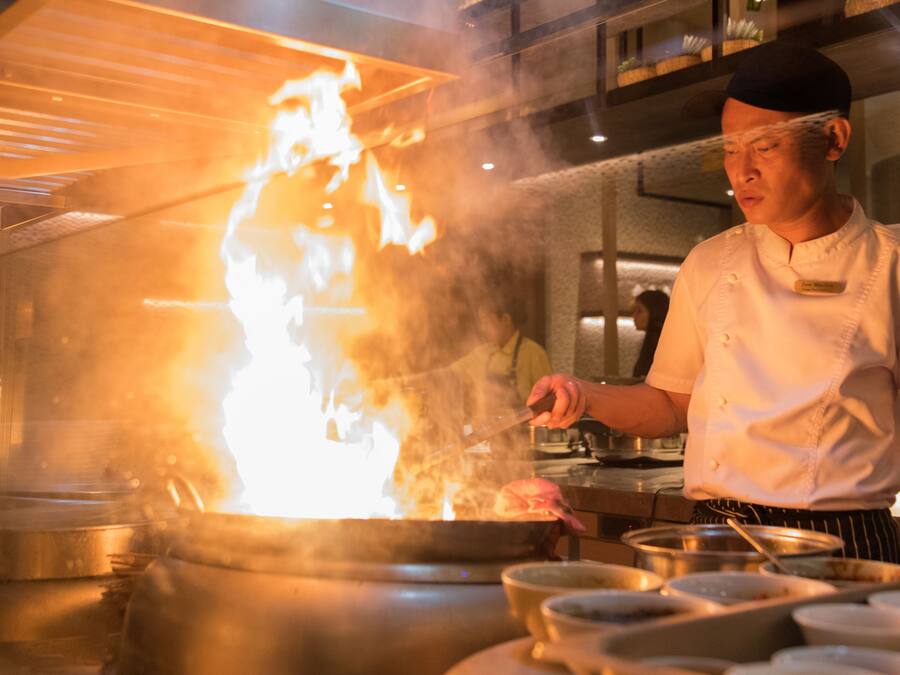 A chef cooking with a large flame in a professional kitchen.