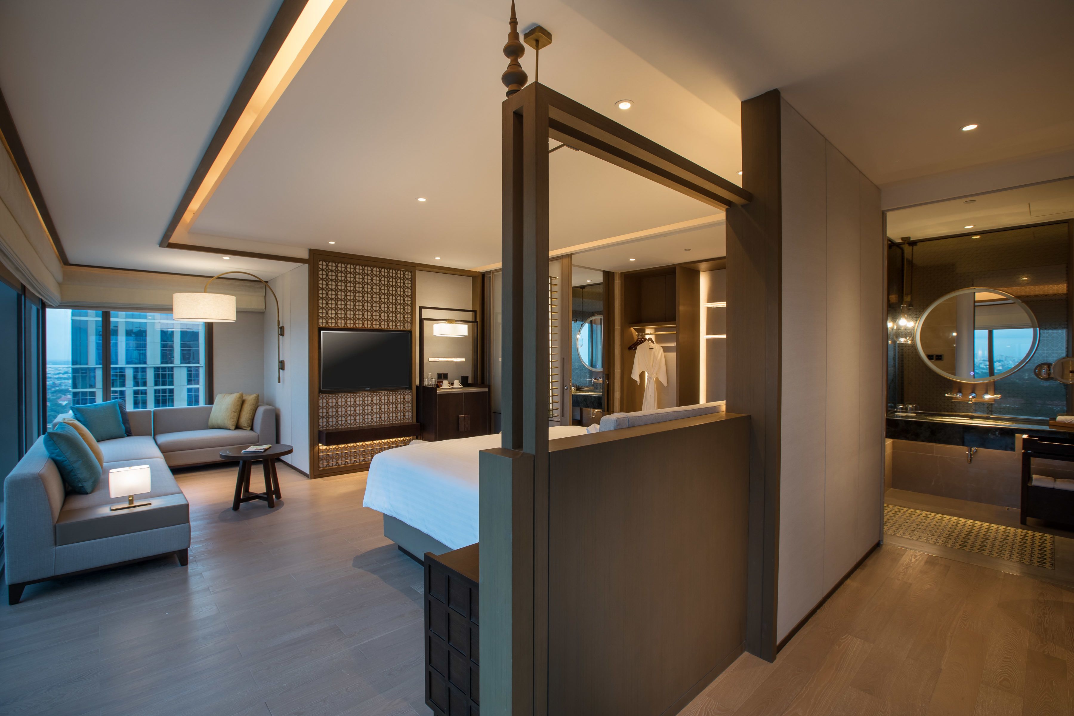 Habitación de hotel moderna con una cama grande, un sofá, un televisor, un baño con espejo y vistas a la ciudad.
