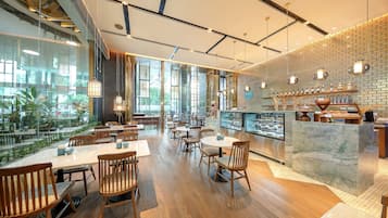 En moderne restaurant med træborde og -stole, en murstensvæg og udsigt til grønne omgivelser.