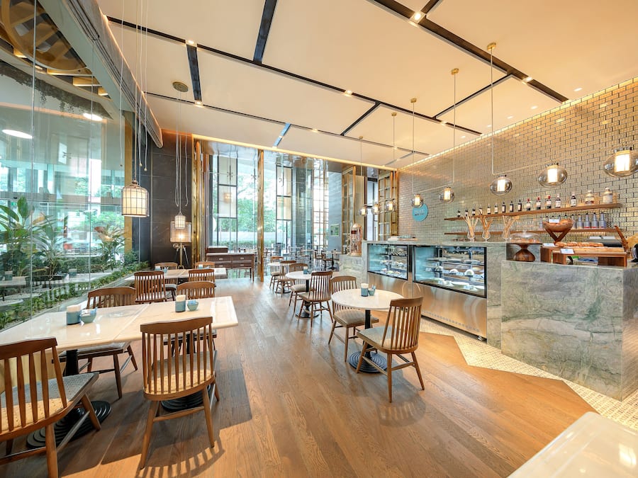 En moderne restaurant med træborde og -stole, en murstensvæg og udsigt til grønne omgivelser.