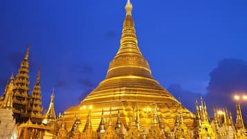 Ein großer, goldener Pagode mit mehreren Stufen und aufwendigen Verzierungen, umgeben von kleineren Gebäuden und einer Menschenmenge.