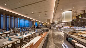 Een moderne hotellobby met een lange receptiebalie, zithoeken en een buffet.