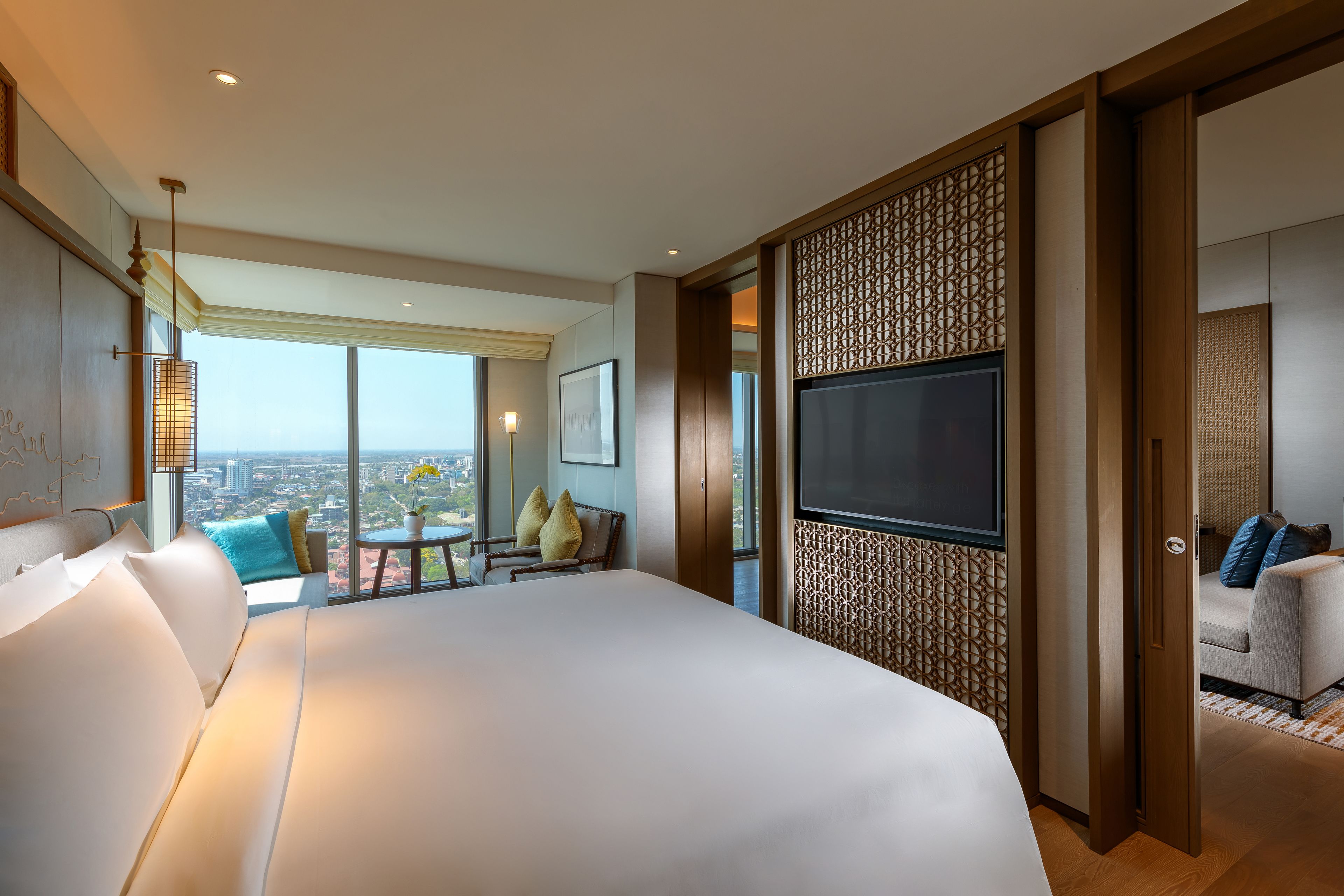 Una habitación de hotel moderna con una cama grande, un televisor, un balcón con vistas a la ciudad y un panel decorativo en la pared.