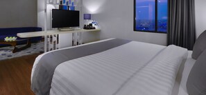A hotel room with a large bed, a desk with a flat-screen TV, a sofa, and a view of the city at night. - Starray Hotel Kebayoran (Jakarta)