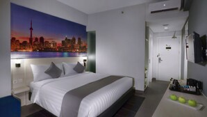 A modern hotel room with a large bed, a cityscape painting on the wall, a small kitchenette, and a bathroom visible through an open door. - Starray Hotel Kebayoran (Jakarta)