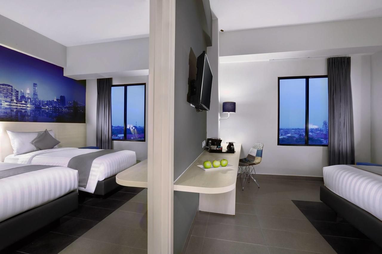 Ein modernes Hotelzimmer mit zwei Betten, einer kleinen Küchenzeile, einem Fernseher und Blick auf die Stadt.