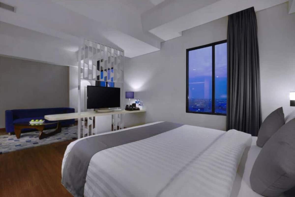 Ein modernes Hotelzimmer mit einem großen Bett, einem Fernseher, einem Schreibtisch und einem Fenster mit Blick auf die Stadt.