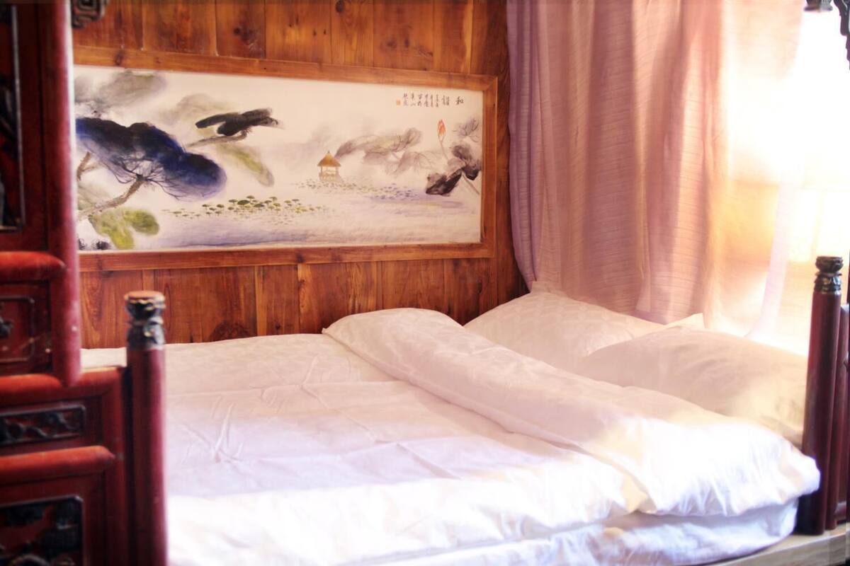 A traditional wooden bed with white bedding, a wooden headboard, and a painting of a landscape with a bird and a pagoda.