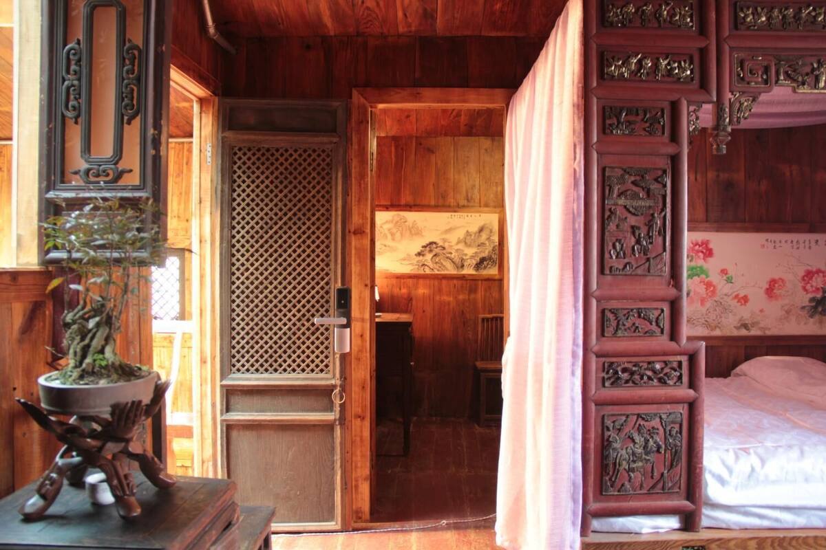 A traditional wooden room with a bed, a door with a lattice design, and a painting on the wall.