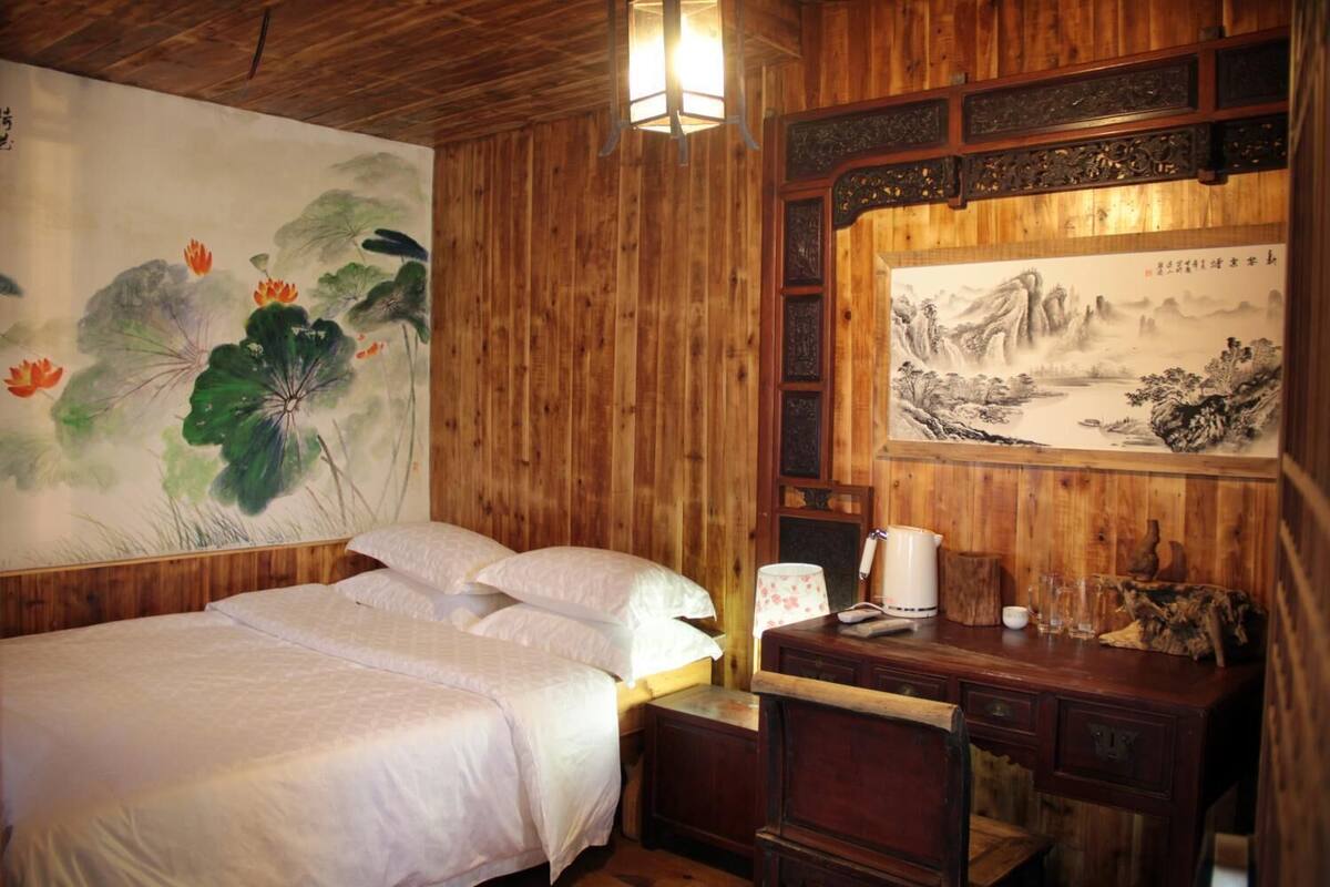 A wooden room with a bed, a desk, and a wall painting.