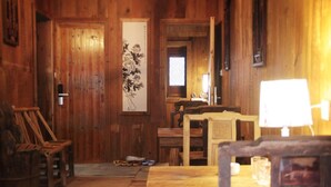 A wooden room with a wooden door, a framed artwork on the wall, a table with a lamp, and a chair. - Huangshan Xishan Wutongqinyuan (Huangshan)