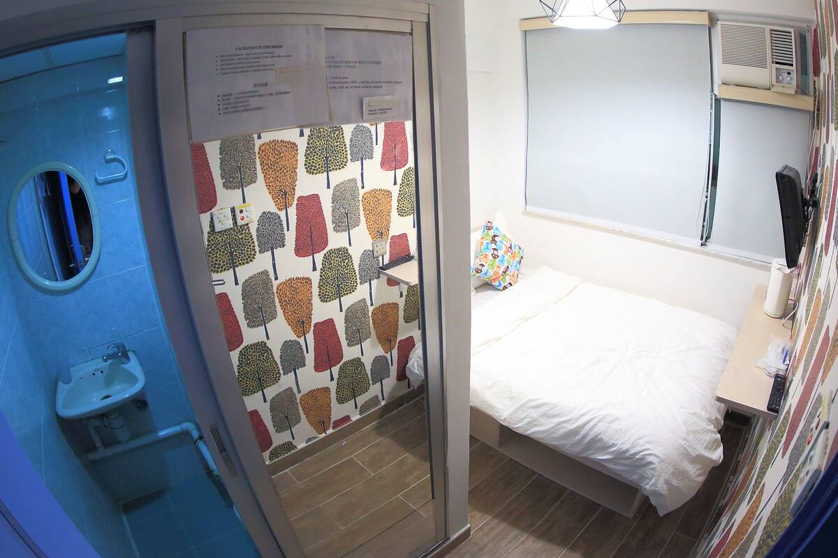 A hotel room with a bed, a small bedside table, a mirror, and a window.