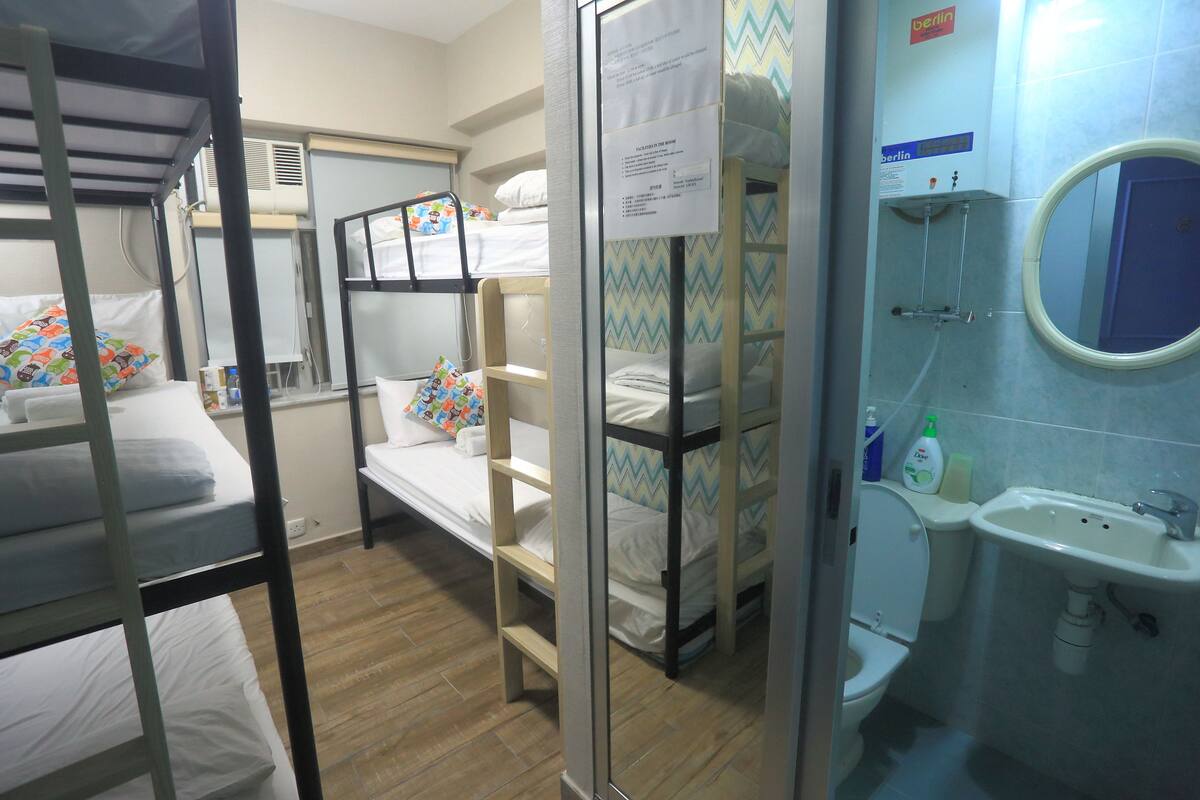 A dormitory room with bunk beds, a bathroom with a sink and mirror, and a notice board.
