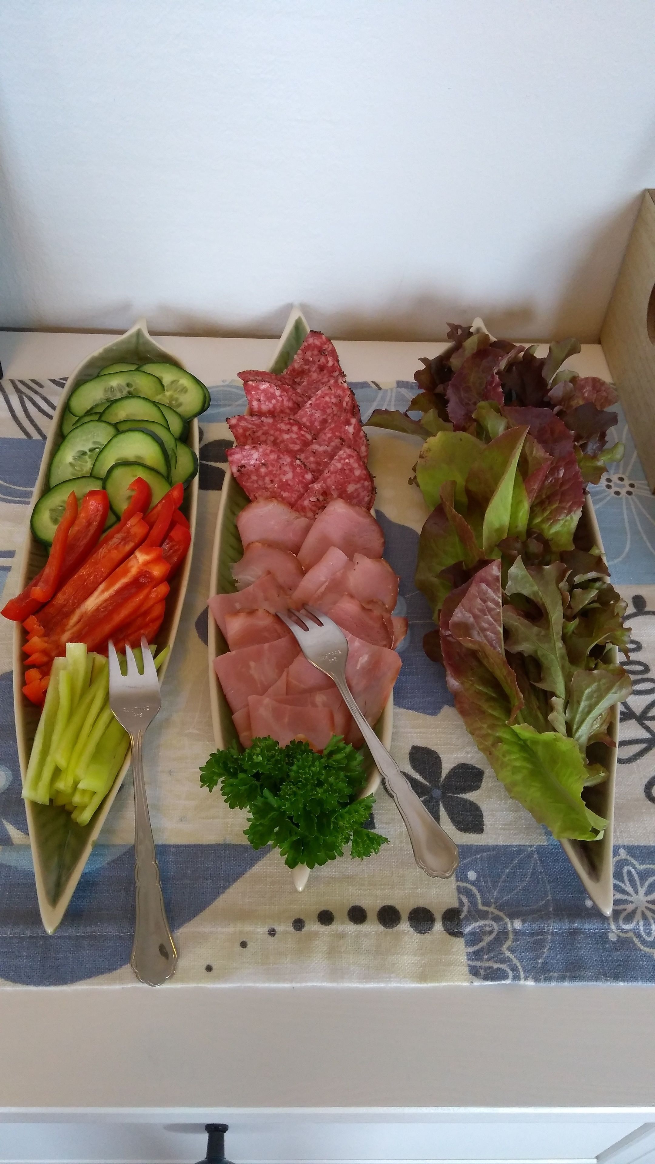 Tres fuentes rectangulares de comida sobre una mesa con mantel estampado.