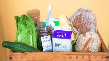 A wooden crate containing a variety of food items including bread, cheese, a jar of jam, and leafy greens.